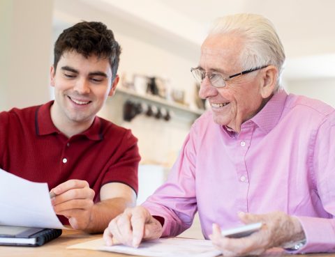 Young Man Helping Senior Neighbor With Paperwork At Home