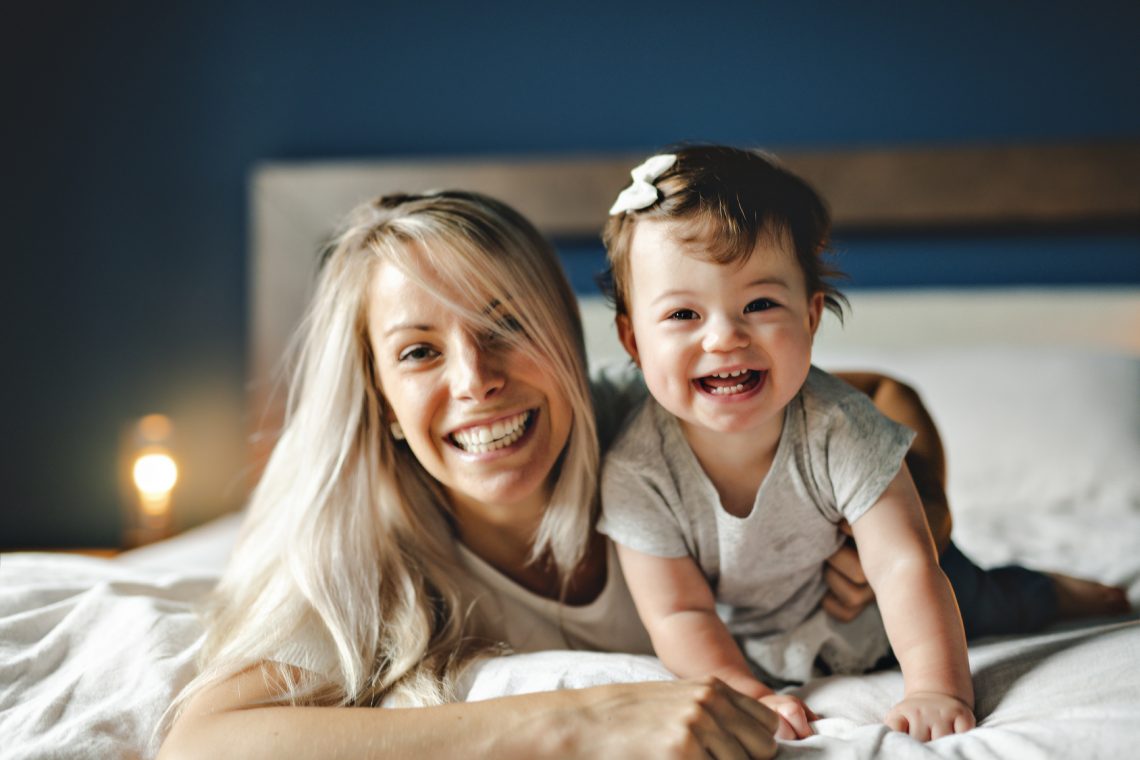 Mother Playing With Baby Daughter In Bedroom At Home