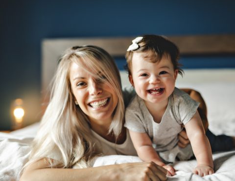 Mother Playing With Baby Daughter In Bedroom At Home